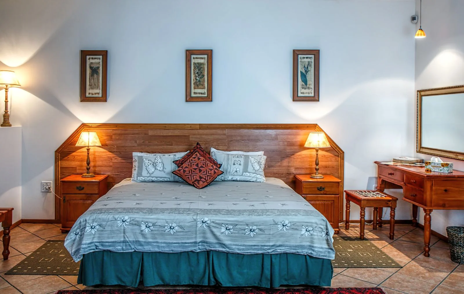 Una cama con colcha azul y cabecero de madera, flanqueada por dos lámparas.